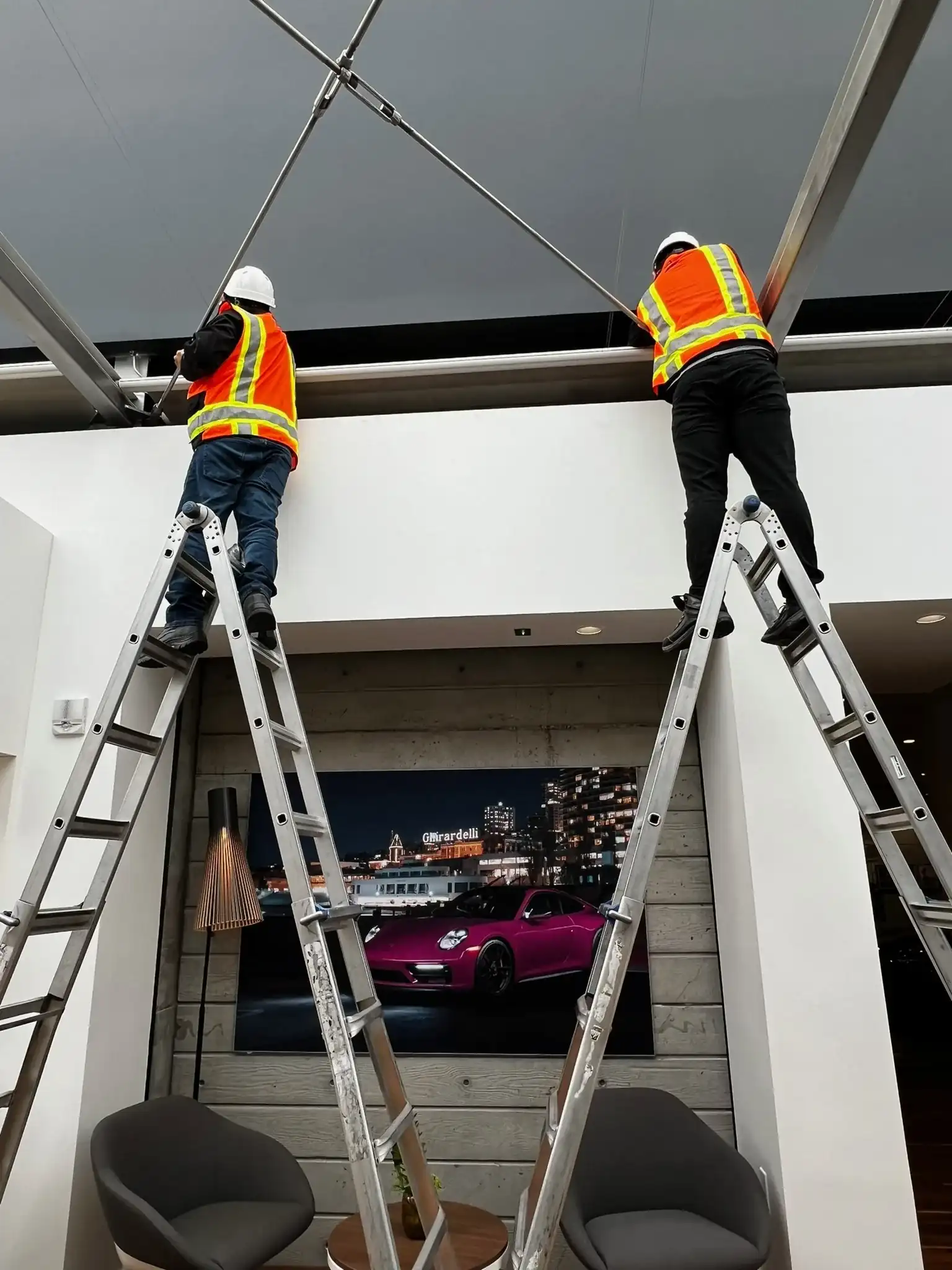 Commercial installation team working from ladders beneath a skylight