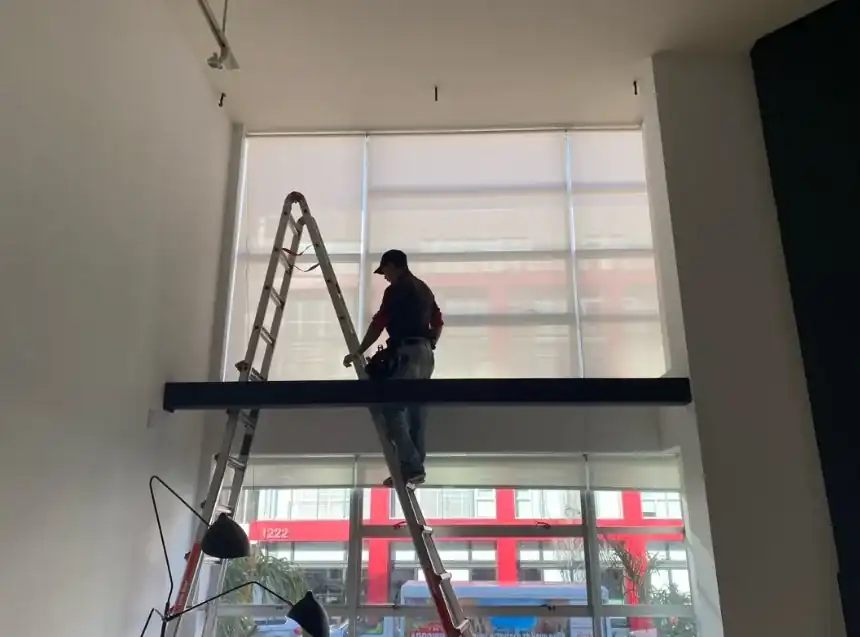 Alro installer installing window coverings at a tall commercial window